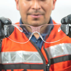 Persona con guantes sosteniendo los lentes de seguridad modelo sencillo por las patillas.
