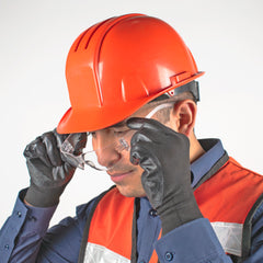 Persona con casco naranja colocándose los lentes de seguridad transparentes modelo sencillo.