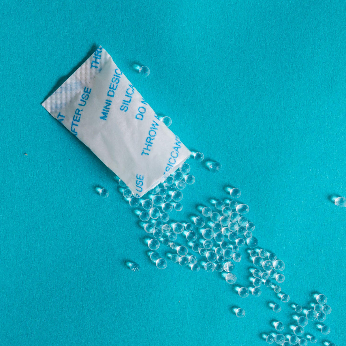 Sobre abierto de silica gel con gránulos transparentes sobre fondo azul.