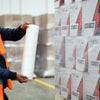 Aplicación manual de película stretch preestirada alrededor de cajas apiladas sobre una tarima.