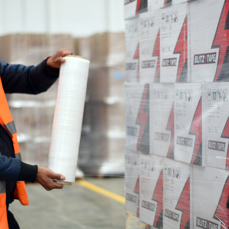 Aplicación manual de película stretch preestirada alrededor de cajas apiladas sobre una tarima.